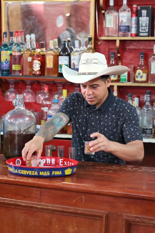 Hombre con sombrero sirviendo mezcal detrás de una barra
